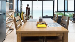 Un espace repas avec une table en bois, des chaises et une vue sur l’océan.