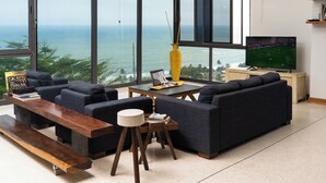 Un salon moderne doté d’une grande fenêtre donnant sur la mer, d’un canapé, d’une table basse et d’un téléviseur.