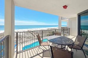 A balcony with a view of the beach, a pool, and a table with chairs. - ORANGE BEACH RETREAT, GREAT VIEW OF THE PASS, GREAT AMENITIES, GREAT FOR FAMILY (Orange Beach)