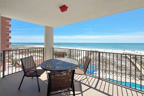A balcony with a table and chairs, overlooking a beach and a pool. - ORANGE BEACH RETREAT, GREAT VIEW OF THE PASS, GREAT AMENITIES, GREAT FOR FAMILY (Orange Beach)