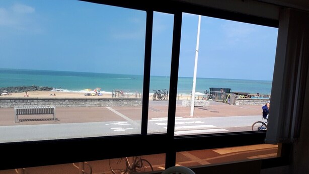 Une pièce dotée d’une grande fenêtre donnant sur une plage, avec une chaise blanche et une table.