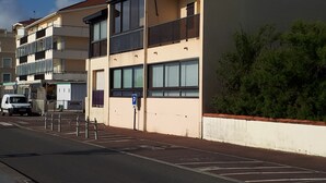 Un immeuble résidentiel à plusieurs étages, doté de balcons, avec un panneau indiquant un espace de stationnement et un fourgon blanc garé devant.