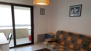 Un salon comprenant un canapé, une table, une chaise, un balcon avec vue et un luminaire suspendu.