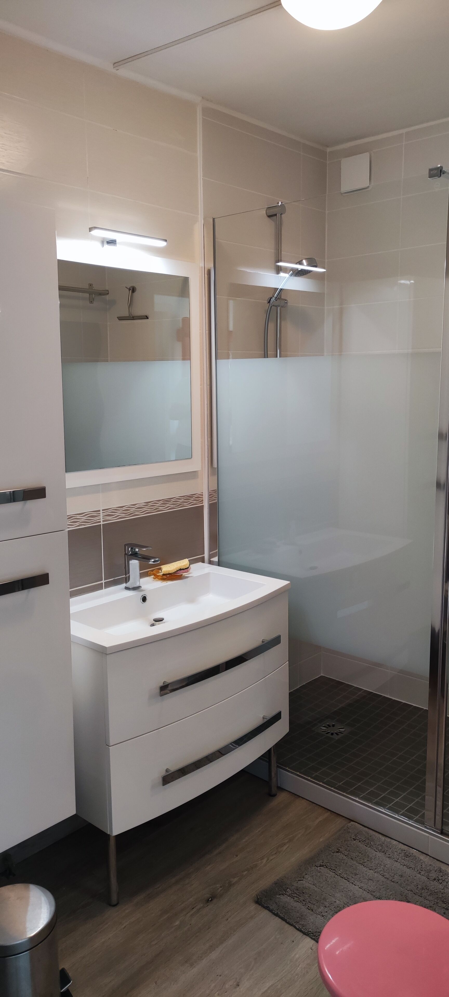 A modern bathroom with a glass-enclosed shower, a white vanity with a mirror, and a red toilet.