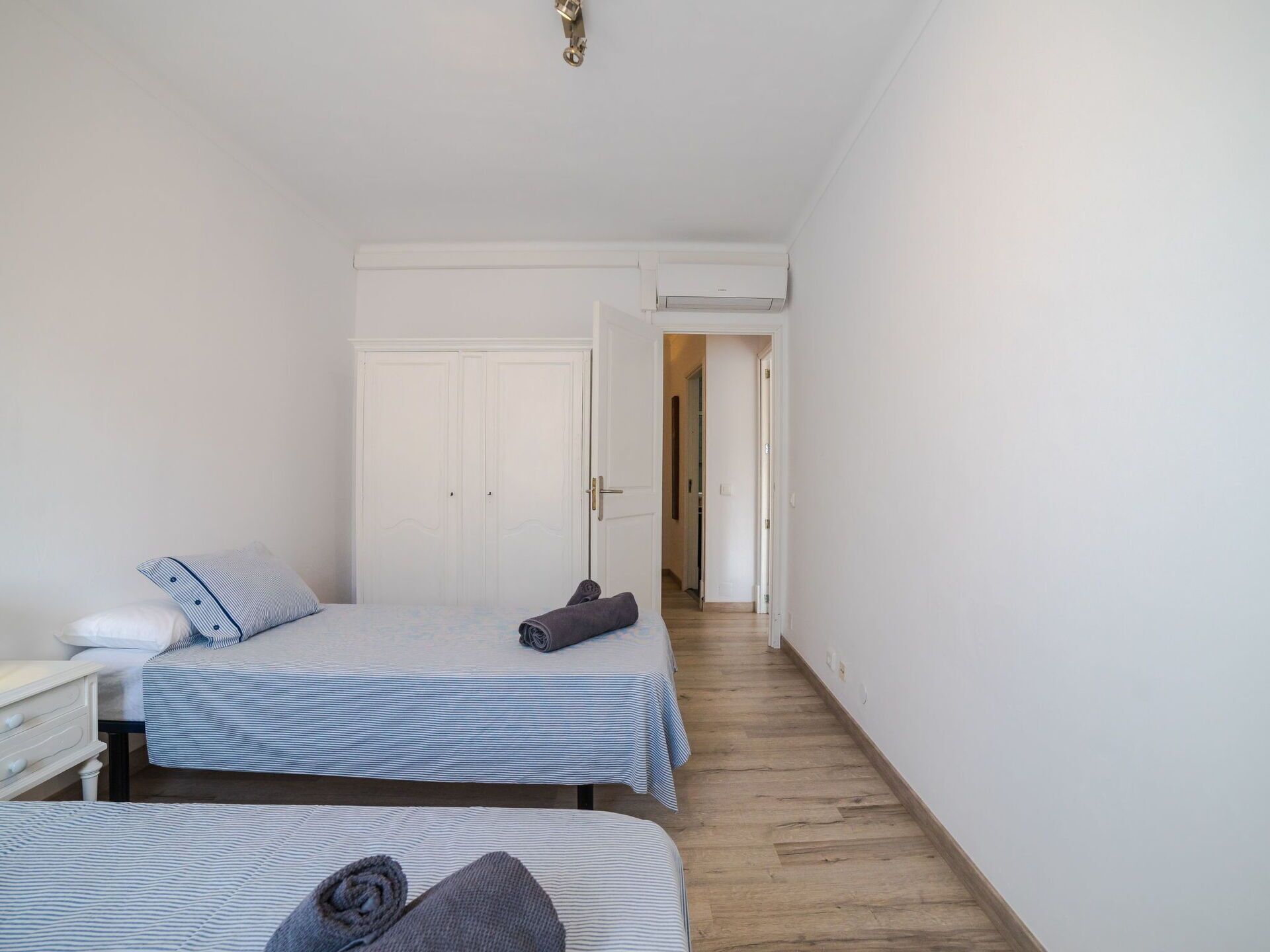 A room with two beds, a white wardrobe, and an air conditioning unit.