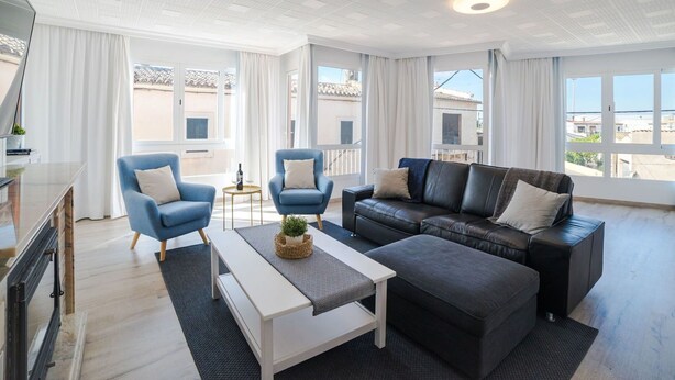 A spacious living room with a modern design, featuring a black leather sofa, two blue armchairs, a white coffee table, and a large window offering a view of the cityscape. - Beautiful apartment for 6 people with A/C, WIFI, TV and patio (Binissalem)
