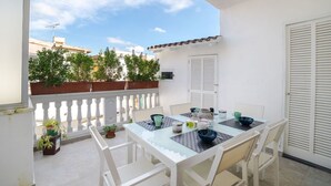 A balcony with a white table and chairs, potted plants, and a view of buildings. - Beautiful apartment for 6 people with A/C, WIFI, TV and patio (Binissalem)