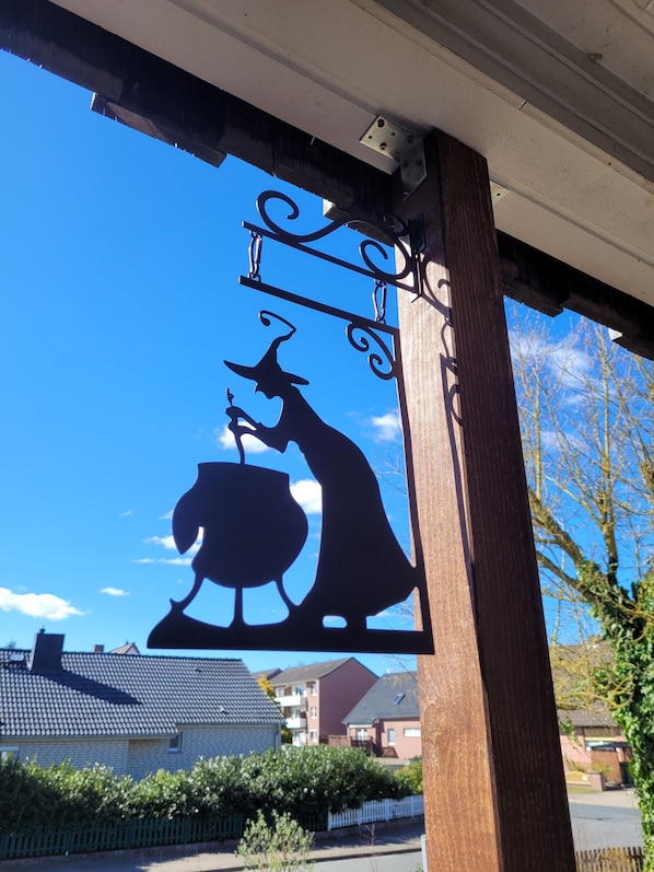 A metal sign with a witch silhouette, a pot, and a staff, mounted on a building's corner. - * NEW DOMIZIL * Very close to nature (Schneverdingen)