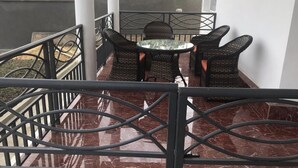 Un balcon doté de meubles en osier et d’une table en verre, entouré d’une rambarde en métal.