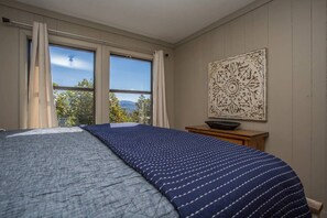 Un dormitorio con una cama, una ventana con cortinas, un adorno en la pared y una mesita con un cuenco.