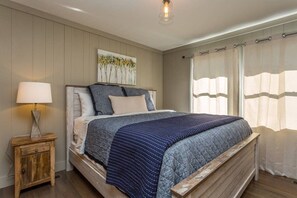 A bedroom with a bed, a bedside lamp, a painting on the wall, and a window with curtains.
