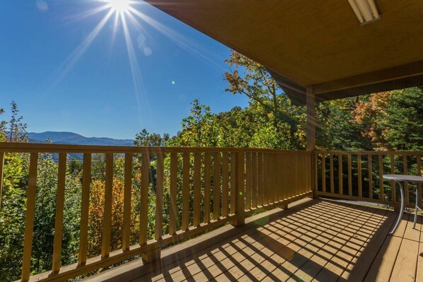 A wooden deck with a railing, a table, and a view of trees and mountains.
