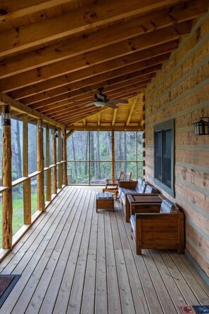 Une terrasse en bois, dotée de bancs et d’un ventilateur de plafond, qui offre une vue sur une zone boisée.