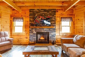 Ein gemütliches Blockhaus-Interieur mit Kamin, zwei Sofas und einem Holztisch.