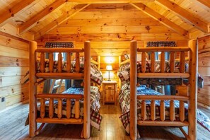 Une cabine avec des lits superposés, des murs en bois et une lampe centrale.