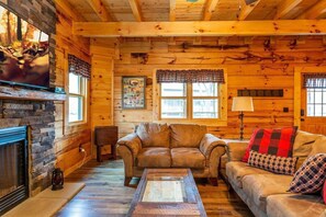 L’intérieur d’une cabane en rondins, avec une cheminée en pierre, des canapés en cuir et un plancher en bois.