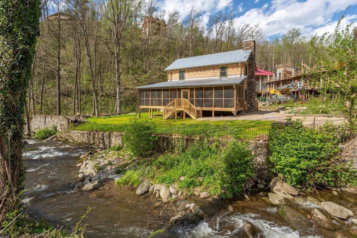 Een rustiek lodge met een gevel van natuursteen, een houten terras en uitzicht op een stromende rivier.