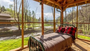 Une terrasse en bois avec un lit, de grandes fenêtres et une vue sur une rivière et la verdure.