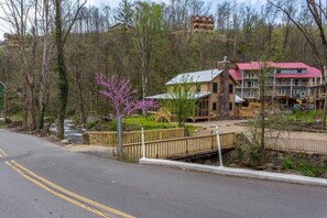 Un immeuble à plusieurs étages, avec un toit rouge, entouré d’arbres et traversé par un petit ruisseau.