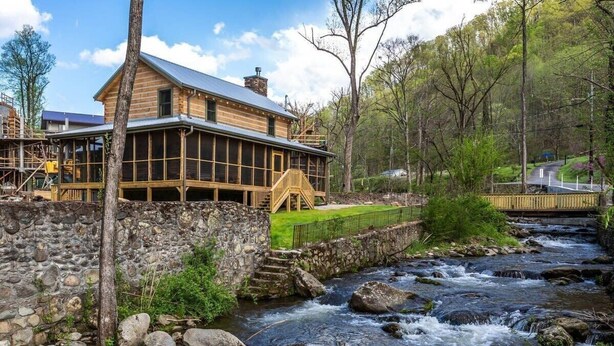 Une cabane en rondins avec des fondations en pierre, une terrasse en bois et une vue sur une rivière qui serpente.