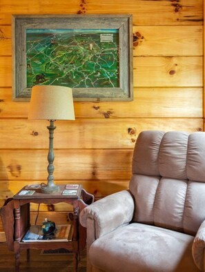 L'intérieur d'un chalet en bois, avec une carte accrochée au mur, une lampe sur une table et un fauteuil rembourré.