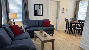 Un salon avec deux canapés bleu foncé, une table basse en bois et un coin repas comprenant une table et des chaises.
