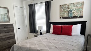 Une chambre à coucher avec un lit, une commode, une table de chevet, une lampe et un tableau accroché au mur.