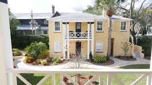 Une maison à deux étages dotée d’un balcon, entourée de jardins bien entretenus et de palmiers.