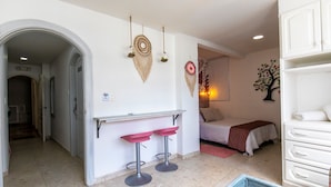 Ein Hotelzimmer mit einem Bett, einem kleinen Tisch, zwei Barhocker, einer weißen Kommode und einer Wanddekoration mit einem Baum.