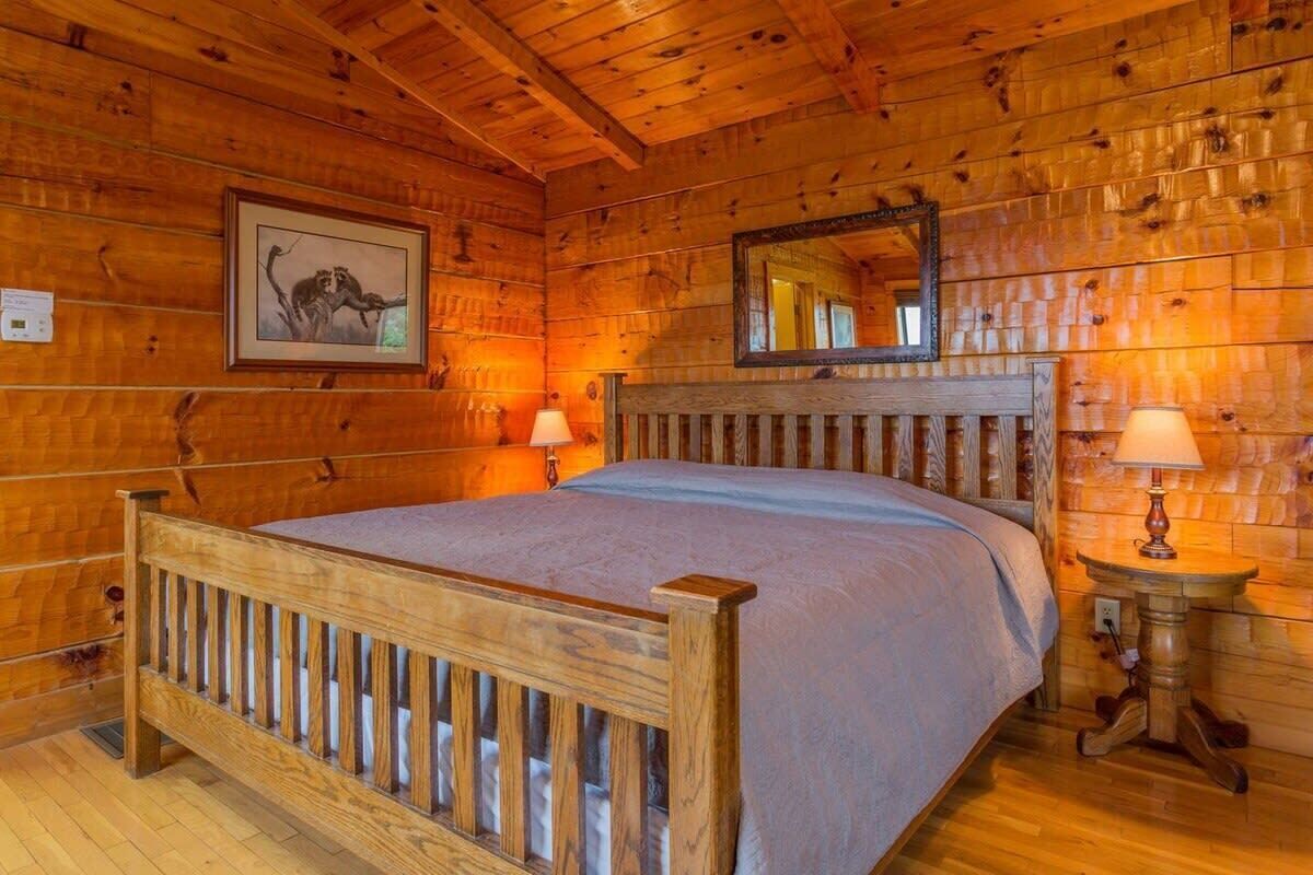 Una habitación de cabaña de madera con una cama, un espejo y dos lámparas fijadas a la pared.