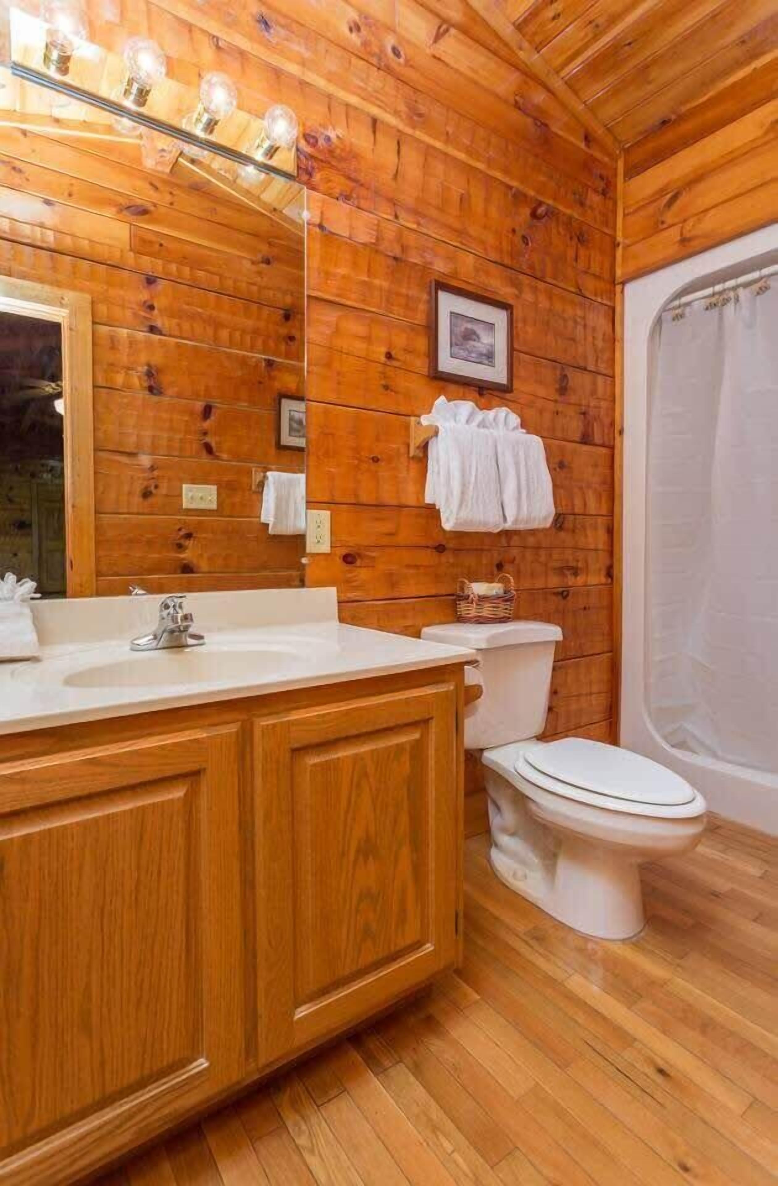 A wooden-paneled bathroom with a wooden vanity, a sink, a toilet, and a shower curtain.