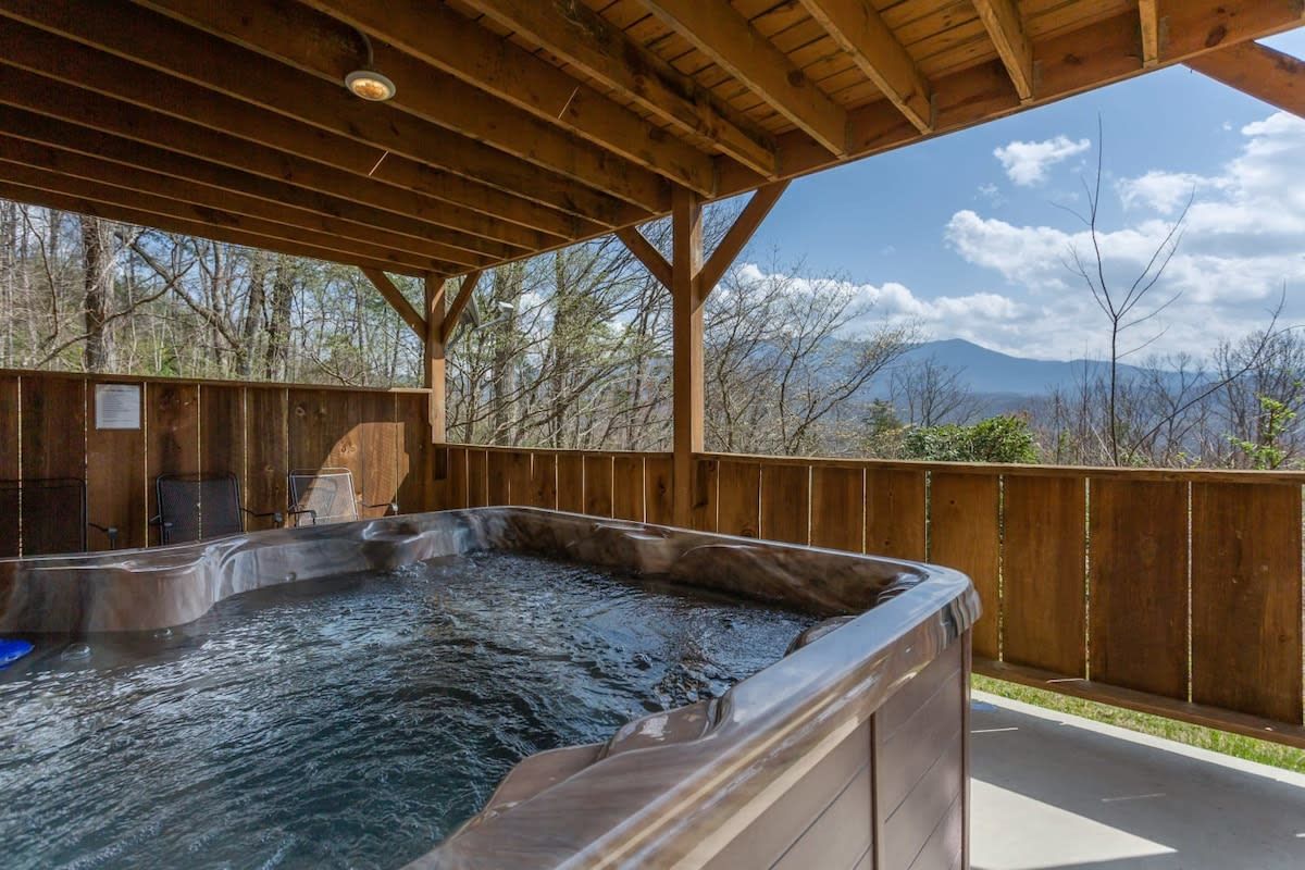 A hot tub under a wooden pergola with a view of mountains.
