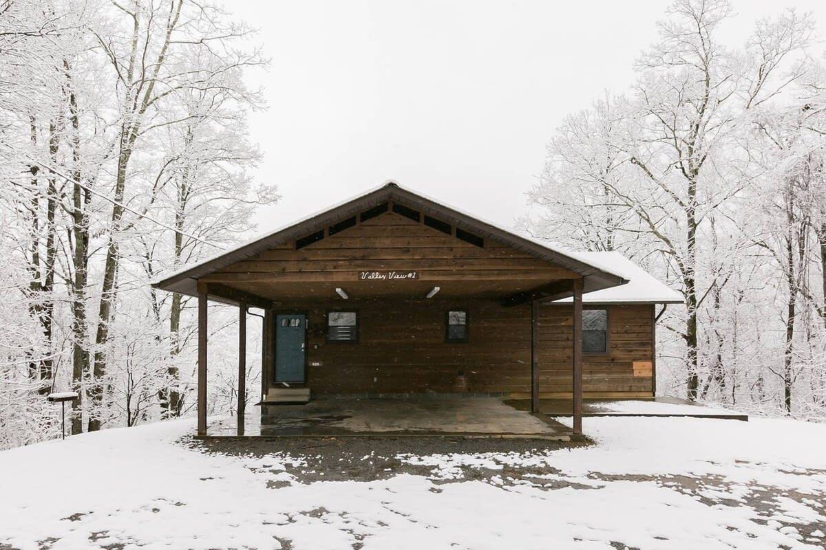 A wooden cabin with a covered entrance, surrounded by snow-covered trees.