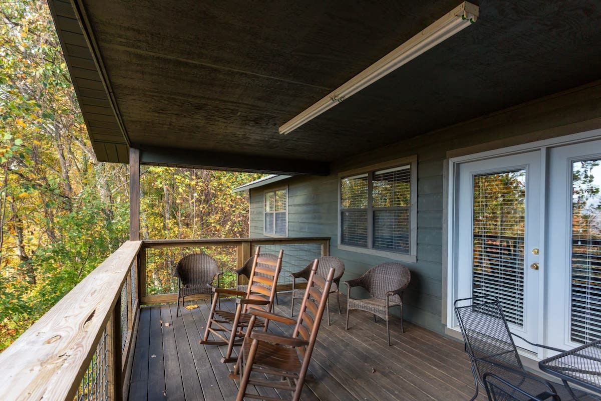 Une véranda couverte avec un plancher en bois, des chaises en métal et une table.