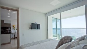 Ein modernes Schlafzimmer mit einem großen Bett, einem an der Wand montierten Fernseher und einem Balkon mit Meerblick.
