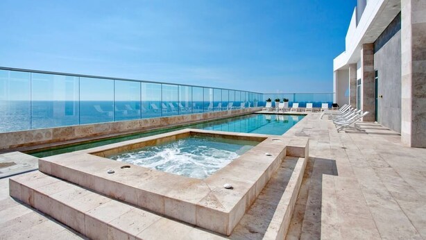 Ein Pool auf dem Dach mit Infinity-Kante, ein Whirlpool, Liegestühle und freie Sicht auf den Ozean.