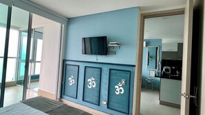 A bedroom with a bed, a TV, and a wall with three framed symbols. - Palmetto Sunset, 20th Floor | 1 Bedroom | Balcony with Ocean View | Laguito, Cartagena (Cartagena)
