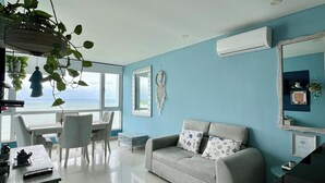A modern living room with a sofa, dining table, chairs, and a hanging plant. - Palmetto Sunset, 20th Floor | 1 Bedroom | Balcony with Ocean View | Laguito, Cartagena (Cartagena)