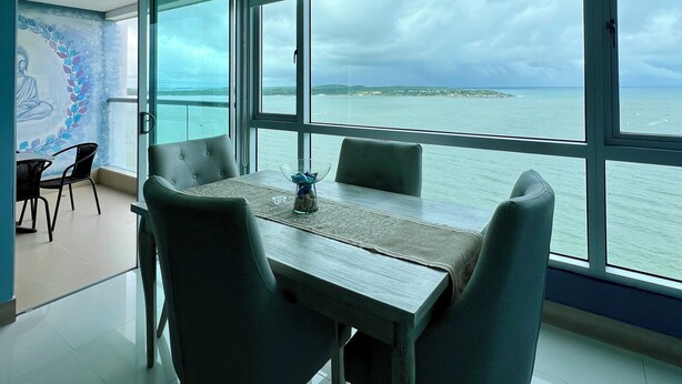A modern dining area with a view of the sea, a glass partition, and a decorative wall. - Palmetto Sunset, 20th Floor | 1 Bedroom | Balcony with Ocean View | Laguito, Cartagena (Cartagena)