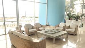 A spacious indoor area with wicker furniture, a large window, and a view of the beach. - Palmetto Sunset, 20th Floor | 1 Bedroom | Balcony with Ocean View | Laguito, Cartagena (Cartagena)