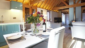 A dining area with a wooden ceiling, a kitchen in the background, and a cozy seating arrangement. - The Barn at Banks Cottage (Pulborough)