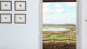 A room with a door leading to a view of a rural landscape, including a body of water and a brick wall. - The Barn at Banks Cottage (Pulborough)