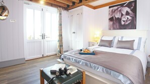 A bedroom with a wooden ceiling, a bed with a striped pillow, a bedside table with a lamp, and a window with curtains. - The Barn at Banks Cottage (Pulborough)
