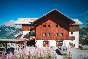 A wooden building with a ski shop, a parking area, and mountains in the background.