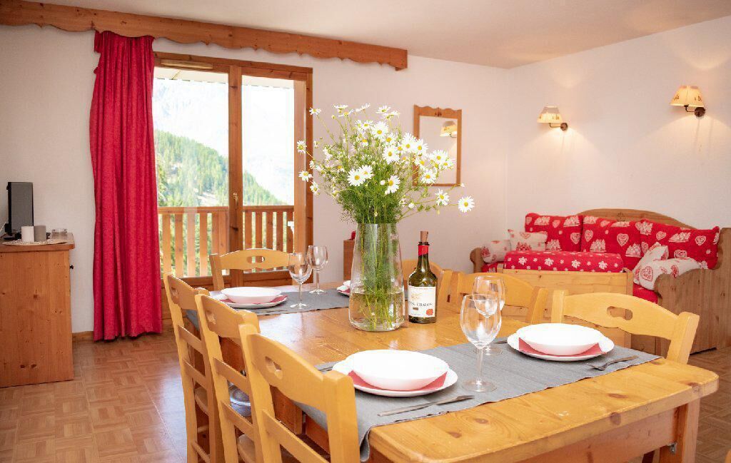 A dining area with a wooden table set for two, a vase of flowers, and a bottle of wine.