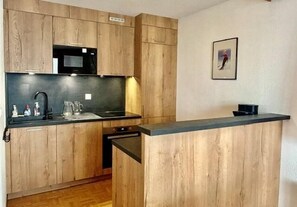 A kitchen with wooden cabinets, a black countertop, a microwave, and a sink. - Wifi, 1st floor, swimming pool, balcony, parking, tv, ski locker, 60m², Puy-Saint-Vincent (Puy-Saint-Vincent)