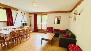 A room with a wooden floor, a dining table with chairs, a sofa, and a window with curtains.