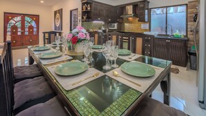 Un coin repas avec une longue table dressée pour le repas, agrémentée d’assiettes vertes, de verres transparents et d’un vase rempli de fleurs.