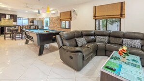 Un salon moderne avec une table de billard, un canapé en cuir et une table basse équipée d’une télécommande.