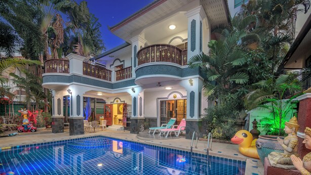 Une grande maison avec une piscine, un balcon et des plantes tropicales.
